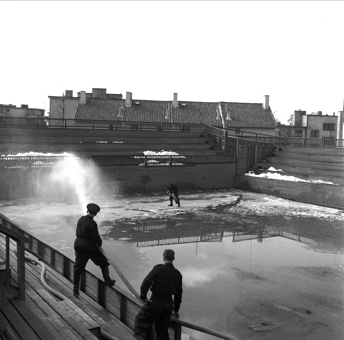 Madserud, Oslo. Menn som spyler idrettsarena med vannslange.