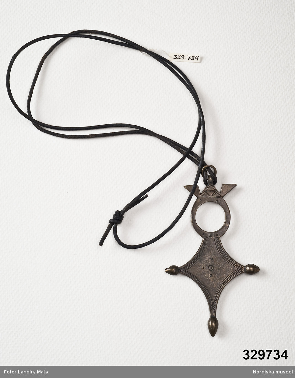 Halsband, smal svart läderrem med hänge i mörk metall korsformig med rund genombruten överdel. Stämpel med texten "Scooter Paris" på baksidan.
/Zingoalla Rosenqvist 2009-02-05