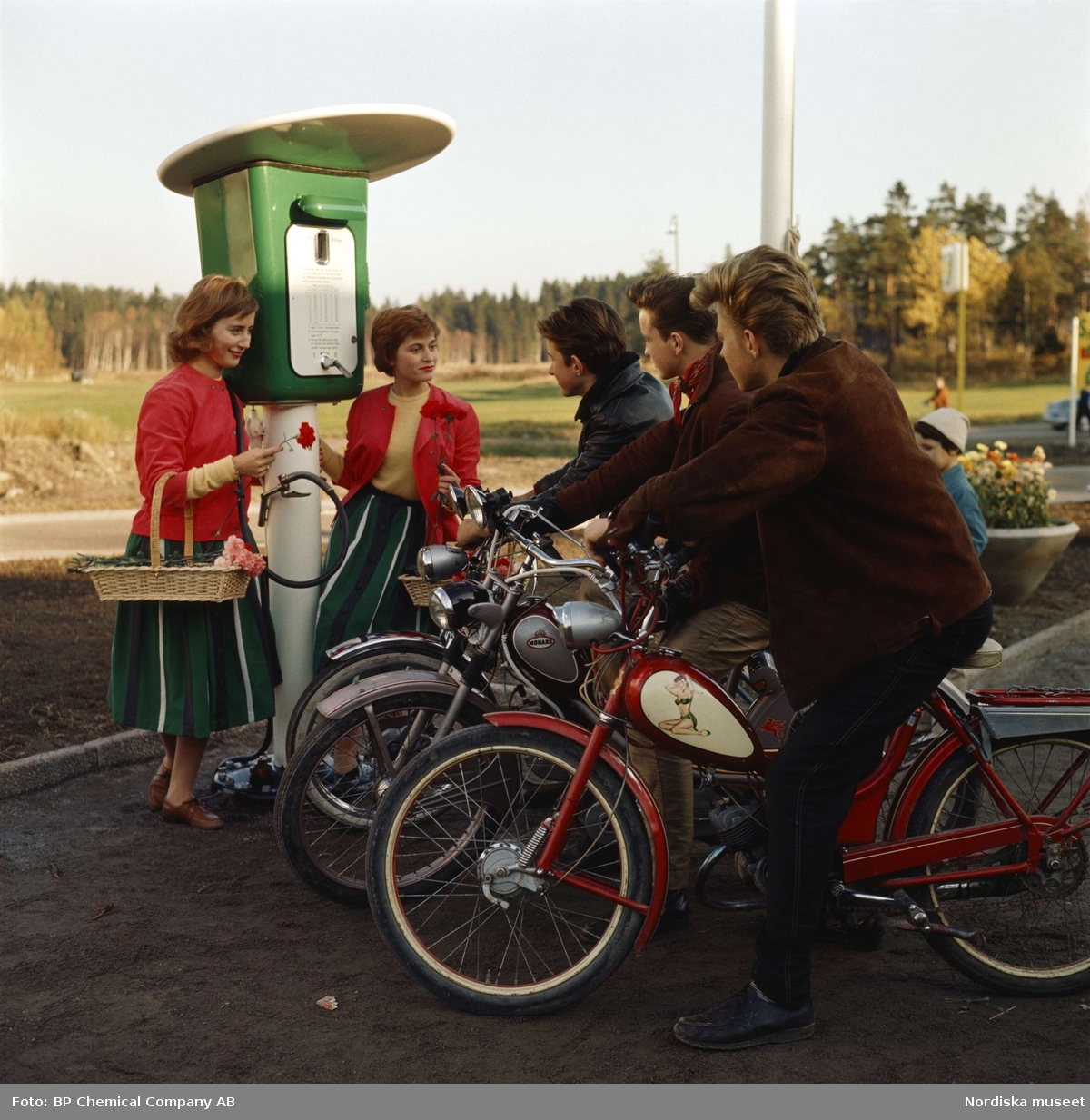 BP-mack. Tre ynglingar på mopeder och två "blomsterflickor" vid bensinstation.