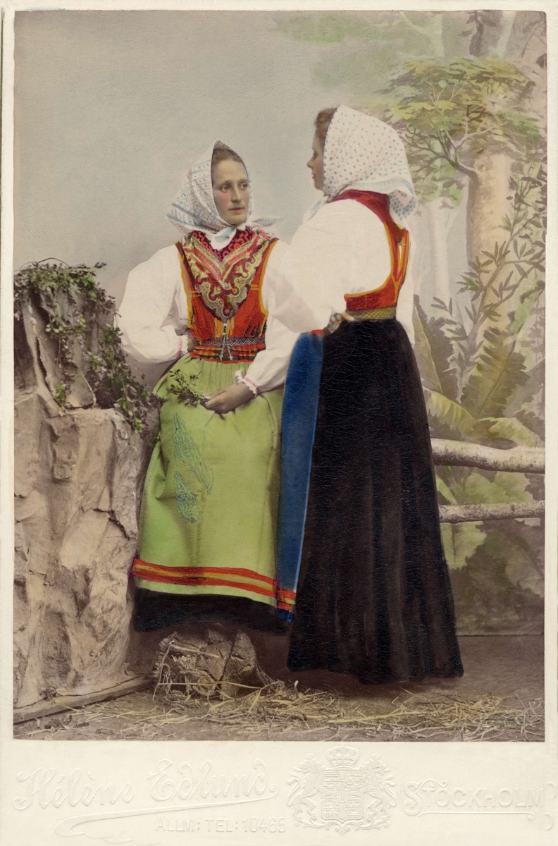 Två unga kvinnor poserar i folkdräkter, med prickiga huvudkläden till