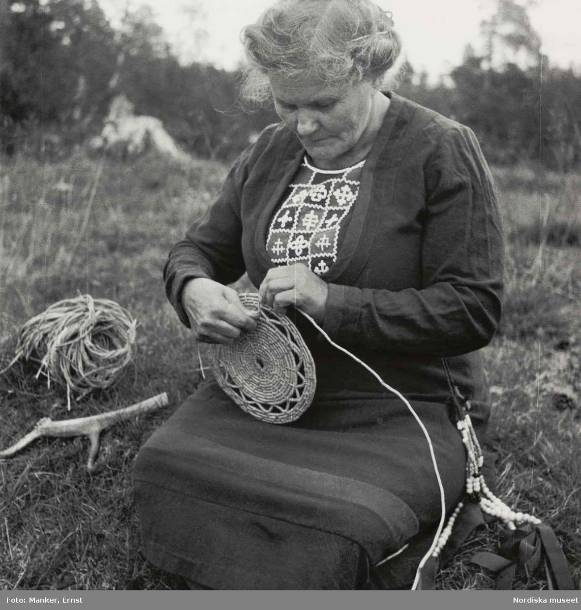 Korgflätning. Maria Larsson (f. Nilsson), dotter till den berömda korgfläterskan Stor-Stina i Glen, flätar en korg.
Mittådalens lappby, Härjedalen, Storvallen. L.A. 820