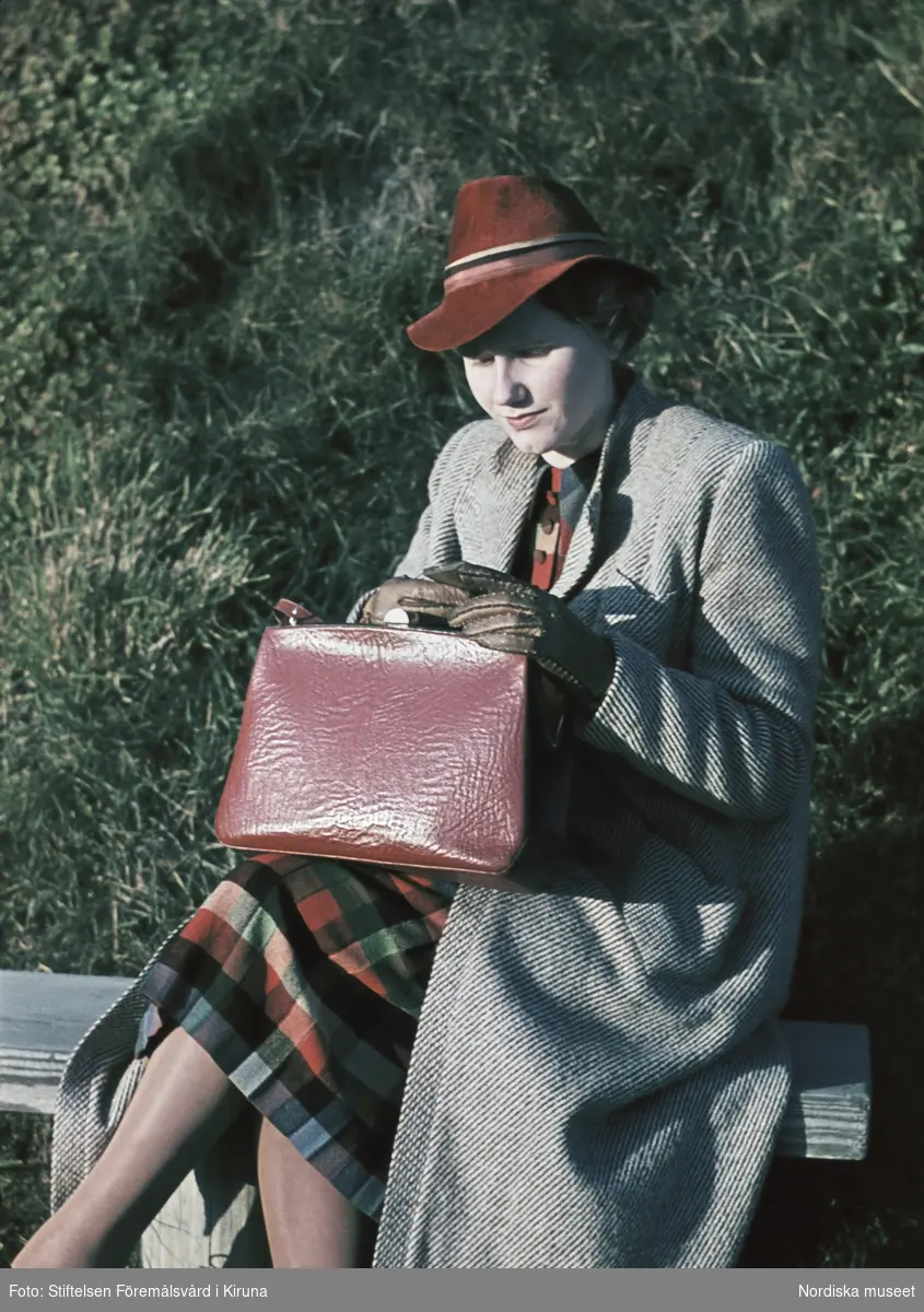 Kvinna i grå kappa, röd hatt och röd handväska.