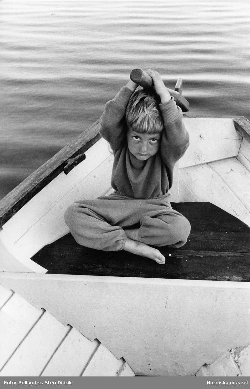 Fotografens son Tom sitter i en båt med rodret över huvudet.