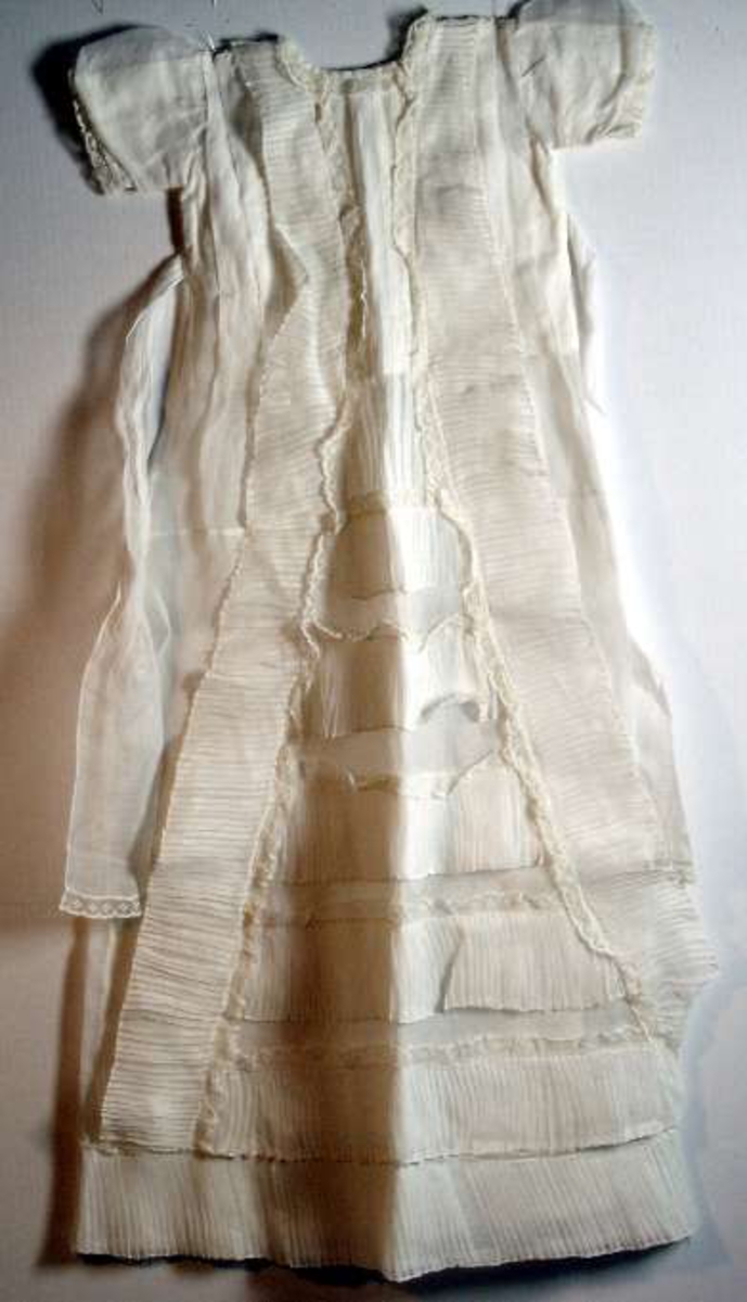 Dopklänning av tunn vit bomullslärft, s.k voile. Spetsar. Knytband i midjan.