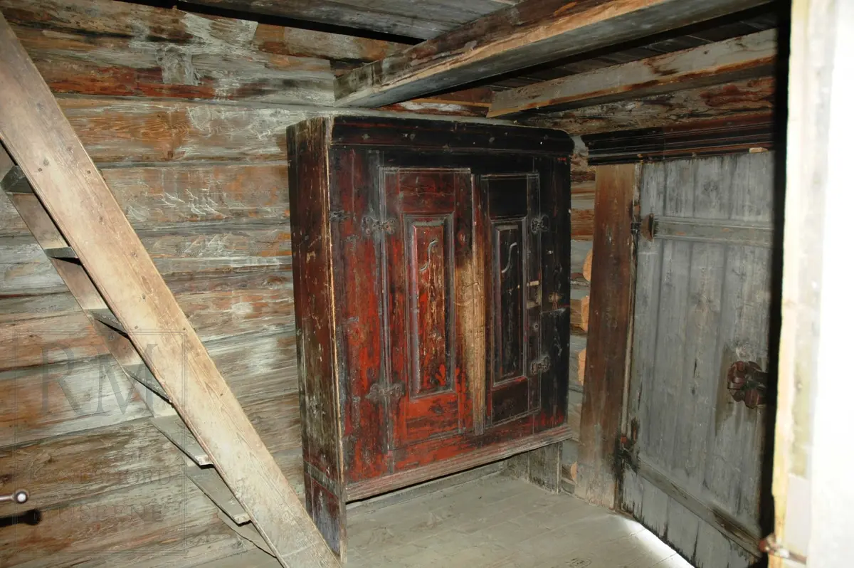 Treroms-stue i laft. Med enkeltkrommet takstein, tidligere torvtak. På gråsteinsmur. På inngangsida går loftet noe lenger ut enn i etasjen under (en-stokks veggsprang). Panelert fremside.