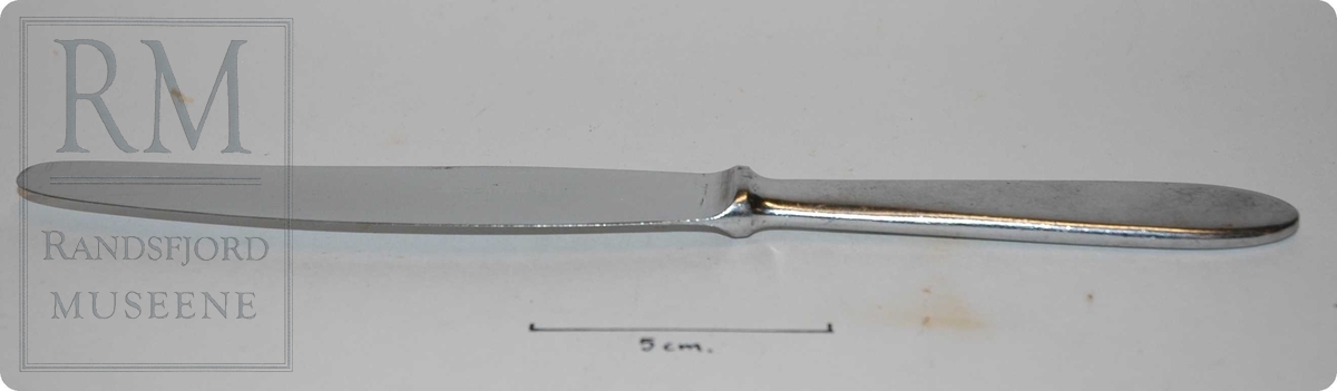 Stål, av et stykke, skaft tilnærmet rektangulært tverrsnitt med avrundede kanter. Forhøyning mellom skaft og knivblad.