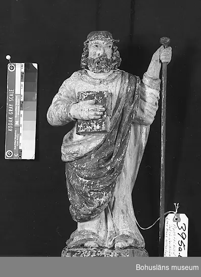 Träskulptur, apostelbild från 1600-talet som tilhör altartavla UM000393.  Förgyllningen som uppvisar båda bladguld, slagmetall och/eller silver.
UM000395a = själva skulpturen,  UM000395b = skulpturens lösa stav.

Enligt katalogkort föreställer skulpturen helgonet och aposteln Jakob den äldre; tillhör altaruppsats UM000393a-i.
Vandringsstaven brukar attribueras till Jakob den äldre.
Krederat trä med mager oljefärg och oljeförgyllning. 

Ur handskrivna katalogen 1957-1958:
Apostelbild, Lane Ryr
H. 39 cm; höger hand håller en bok, vänster en stav b) L. 39,5 cm. Färgen delvis flagn.; små bitar avslag.

Lappkatalog: 13

Se foto på föremålet i Uddevalla museums kyrkliga utställning 1920, UMFA53292:0013

Ur Nationalencyklopedin, NE.se:  Apostel
I konsten framställs apostlarna alltid barfota samt klädda i tunika och mantel. De bär oftast en bok samt sitt individuella attribut, i allmänhet respektive martyrredskap (Petrus bär dock himmelrikets nycklar).