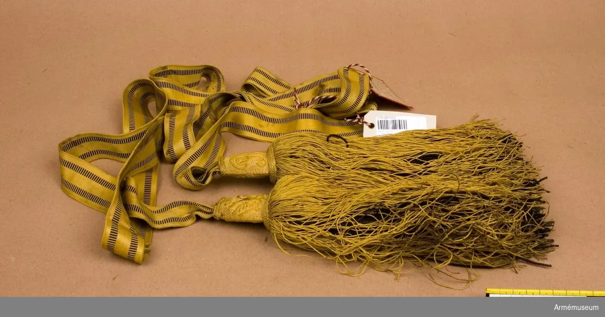 Grupp C I.
Paradskärp av gult silke, vävt med två svarta ränder på sidorna. Tofsar; övre delen är av trä och klädda med gult tyg och broderi i gult silke på ena sidan med dubbel örn och den andra namnchiffer "F.I. I" =Kejsar Franz Josef I. Nedre delen består av snören, l: 250 mm - de inre av svarta, tjocka snören och de yttre av gula, tunna.

Skärpet och tofsarna har några fläckar, troligen av blod. 

LITT  Adjustirungs-Ausrüstungs (Vorschrift) für das K.K. Heer, I Theil, Wein 1871. Sida 111, 112,.Feldbinde. Bestämmelser och mått för officerarnas paradskärp vilkas längd är dubbelt kroppens omfång.