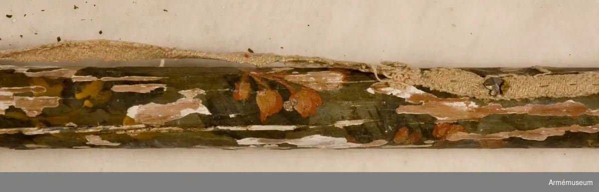 Stångens övre del bemålad med blomornament på mörkblå botten. Äpple med guldspår och konturer av bladornament. Nedre delen av stången målad i gult.
Påklistrad lapp med uppgift om att fanan tagits i Narva 1700.