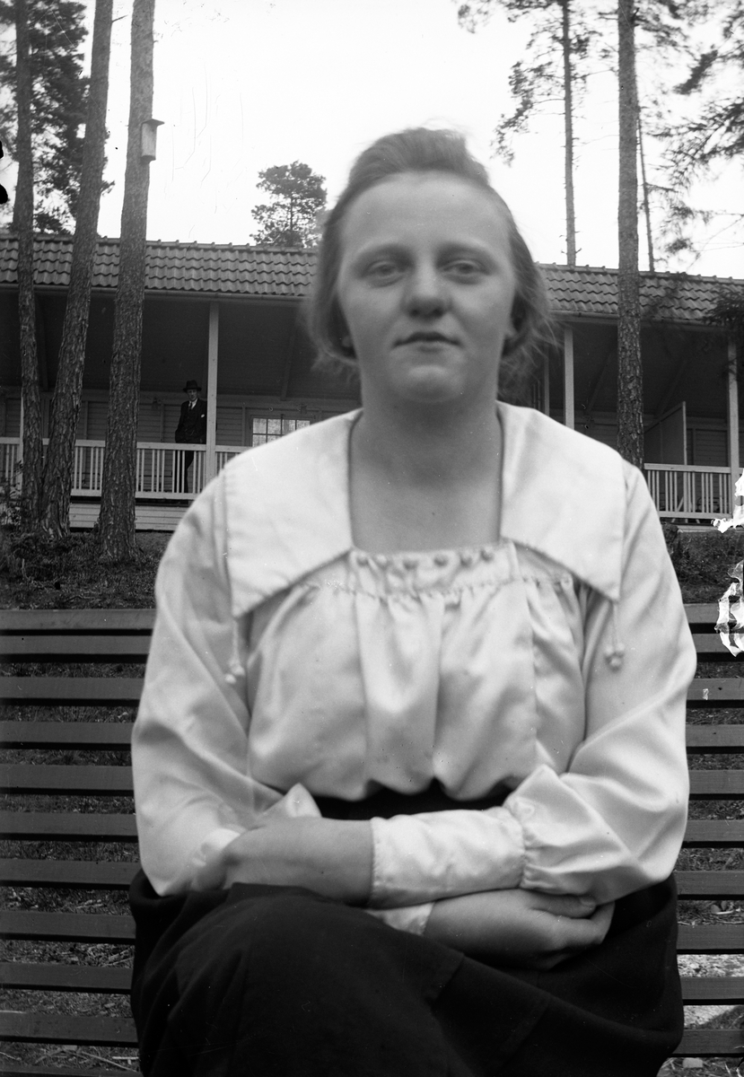 Lungkliniken i Eksjö. En kvinna med korslagda armar sitter på en bänk, i bakgrunden syns en träveranda.