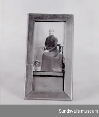 Fotografi i visitkortsformat i träram. Enligt anteckning ska fotografiet föreställa Märta Moberg sittande på en stol med en hund vid sina fötter.