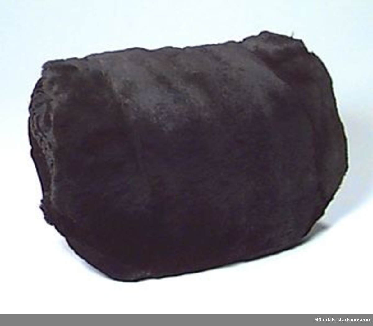 Muff med brunsvart päls som på baksidan möts av svart sammet. På baksidan finns en ficka som går att öppna/stänga med en dragkedja.