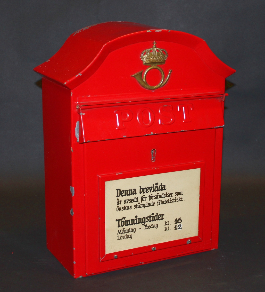 Brevlåda av modell Östberg, målad i rött och med ett handtextat anslag: Denna brevlåda är avsedd för försändelser som önskas stämplade filatelistiskt. Tömningstider, Måndag - Fredag kl 16, Lördag k 12.