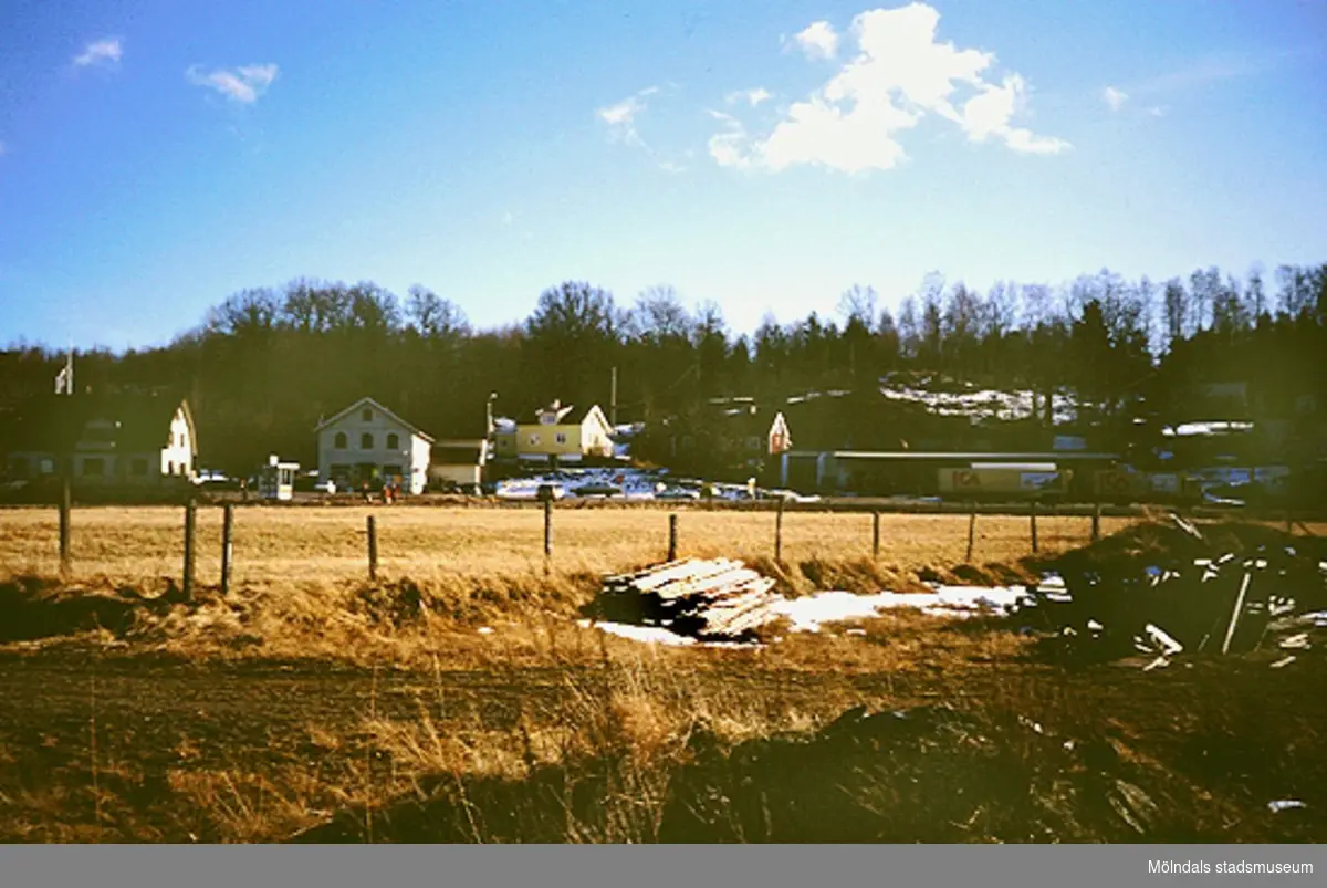 Jordbrukslandskap och ängsmark, mars 1994. I bakgrunden ses villor och en långtradare med släp från ICA.