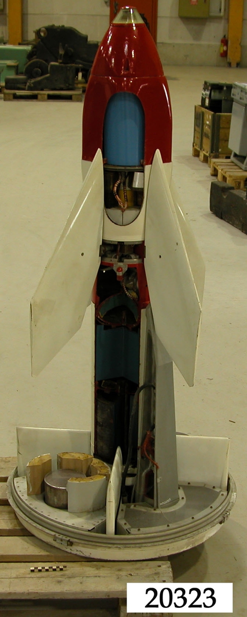 Luftvärnsrobot, vit kropp av plåt, vita fenor av plast. Röd topp och mitt.
Robotens kropp ituskuren längsgående för demonstration.
Till roboten hör skyddshölje av vit plast.