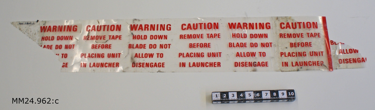 Genomskinlig tejpremsa med röd text längs hela.

WARNING                          CAUTION
HOLD DOWN                    REMOVE TAPE
BLADE DO NOT                  BEFORE
ALLOW TO                      PLACING UNIT
DISENGAGE                    IN LAUNCHER