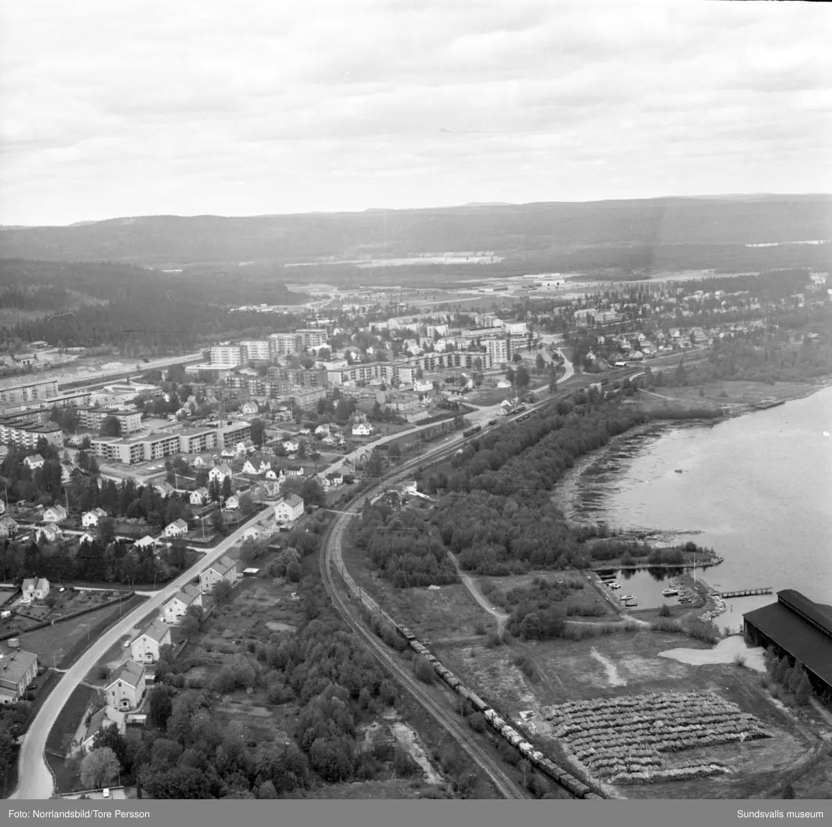 Flygfoton över Timrå med omnejd. Centrum, industriområdet, idrottsplatsen med "Grytan" och isladan, Östrandsfabriken, Vivstavarvstjärn, landsbygd.