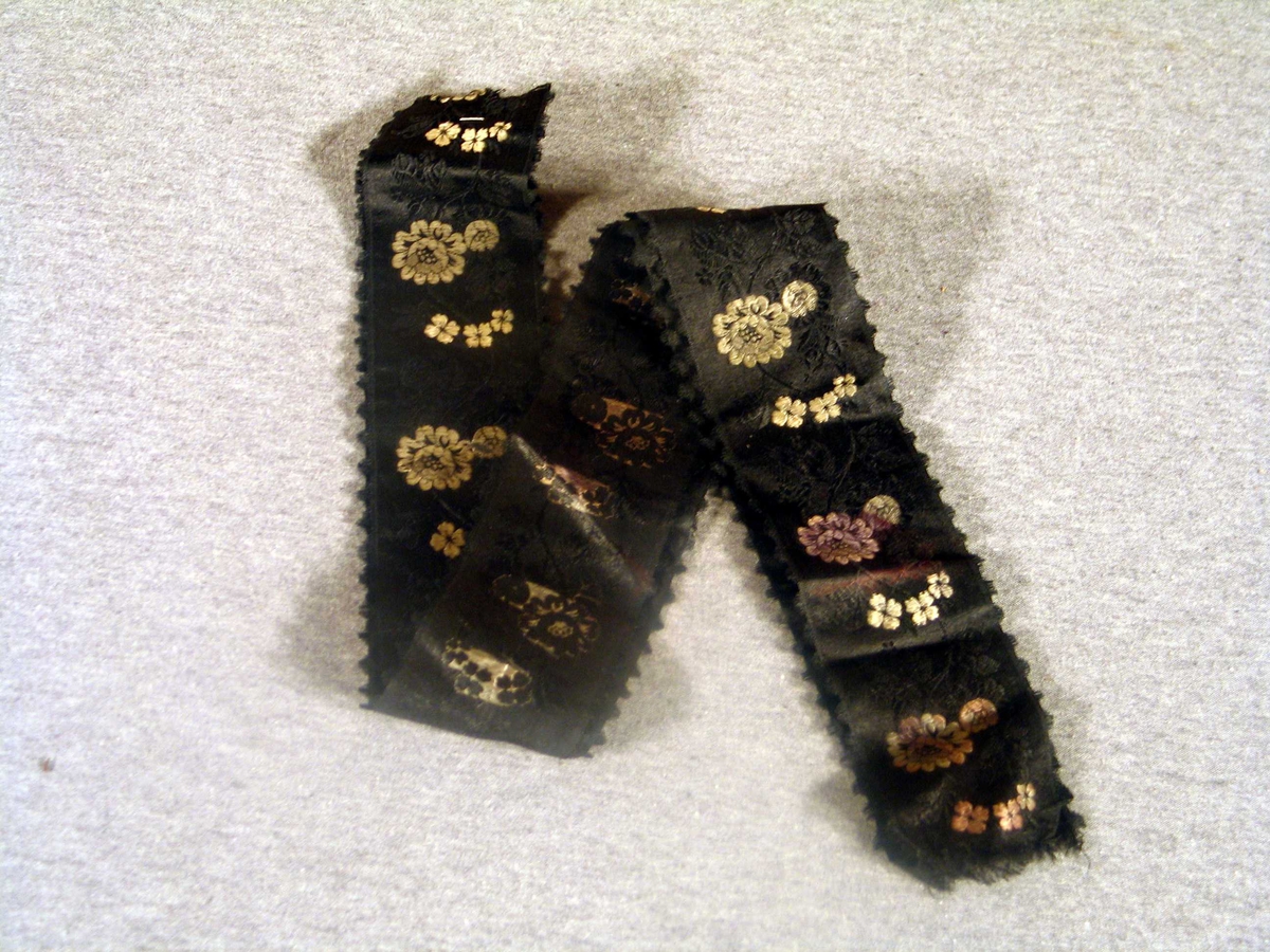 Svarte silkeband med brosjerte blomar kvitt og svart. 
2 stk.