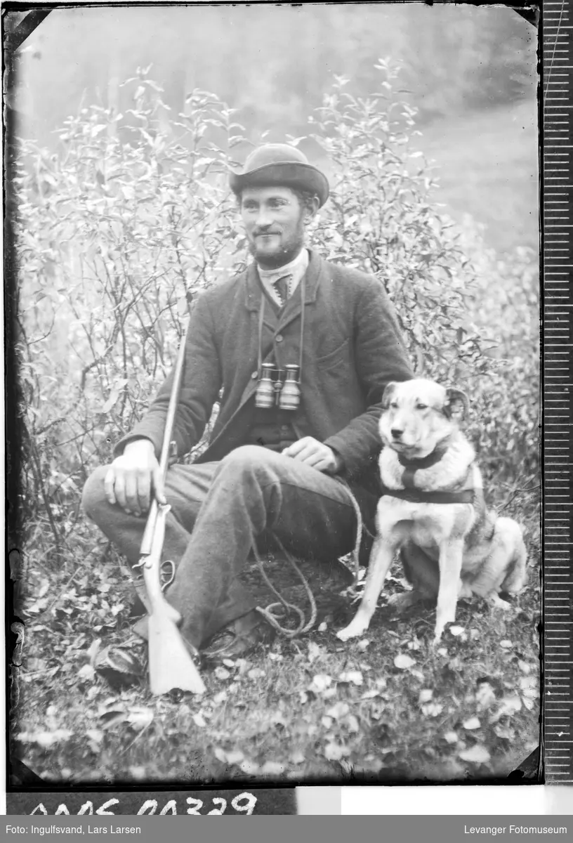 Portrett av mann med kikkert, gevær og en hund.