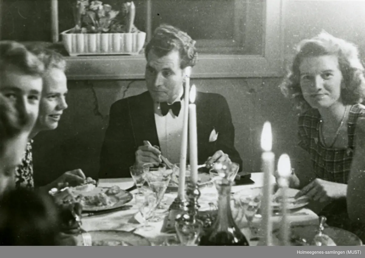To kvinner og en mann ved et middagsbord dekket til fest.