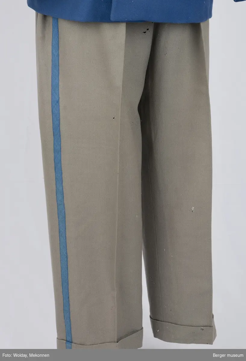 Buksene er grå med en kornblå stripe nedover fra linningen fra begge sider. Buksene har sidelommer, baklomme og en liten lomme foran. Linningen er foret.