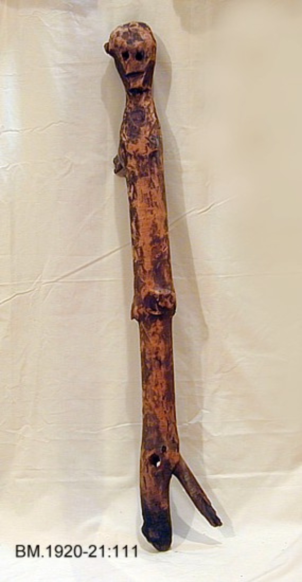 Fra protokollen: 2 husgudar (111 og 112) av gran, funne nedstungne i gormyr, saman med attributtar (3 tresnabbar). Nærmare "beskrivelse" av figurar, attributtar og fundtilhøve i R. Berge, Husgudar i Noreg (1921).
Trestokk formet som menneskelignende figur.
