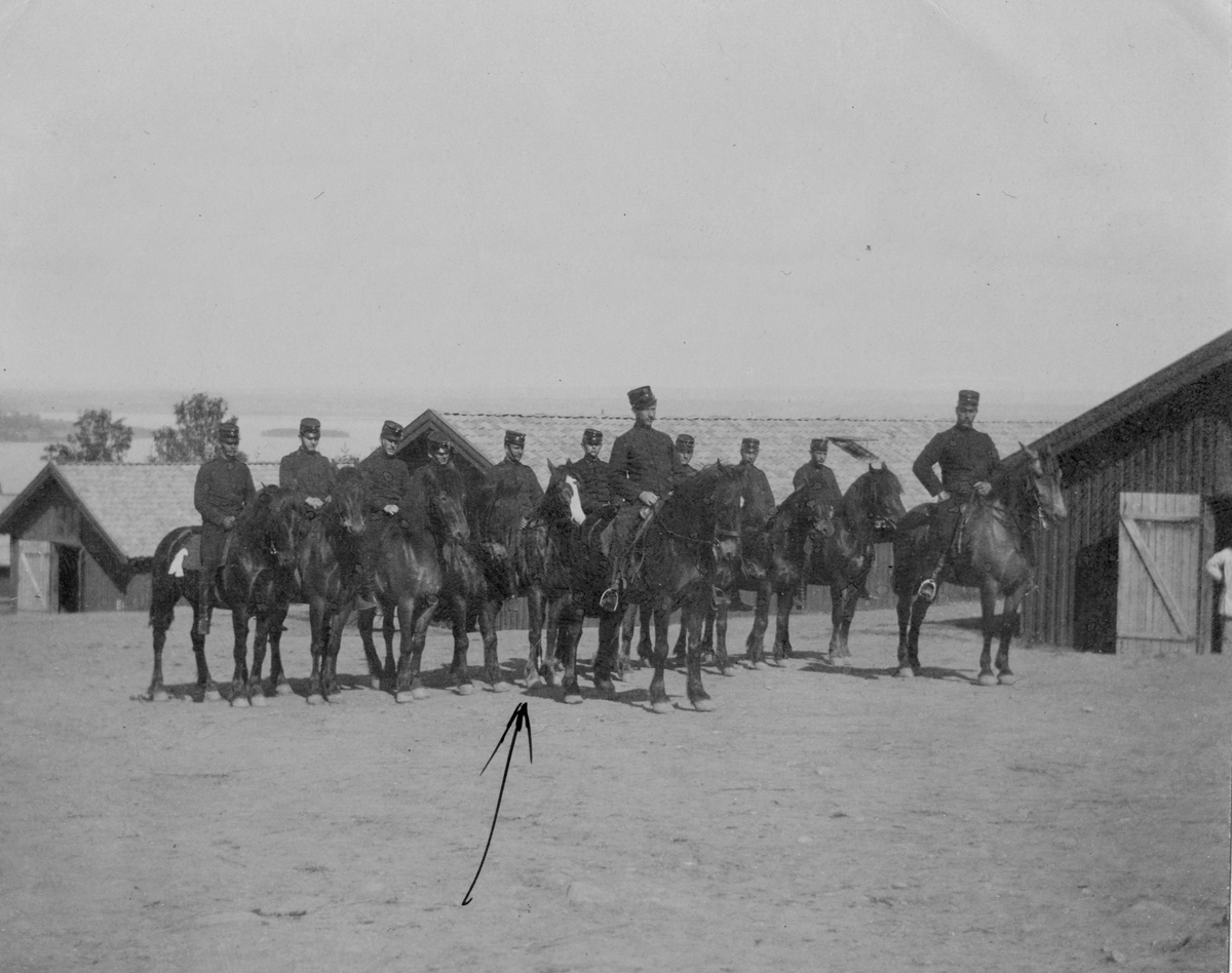 Elleve menn til hest, trebrakker i bakgrunn. Starum leir sommeren 1900