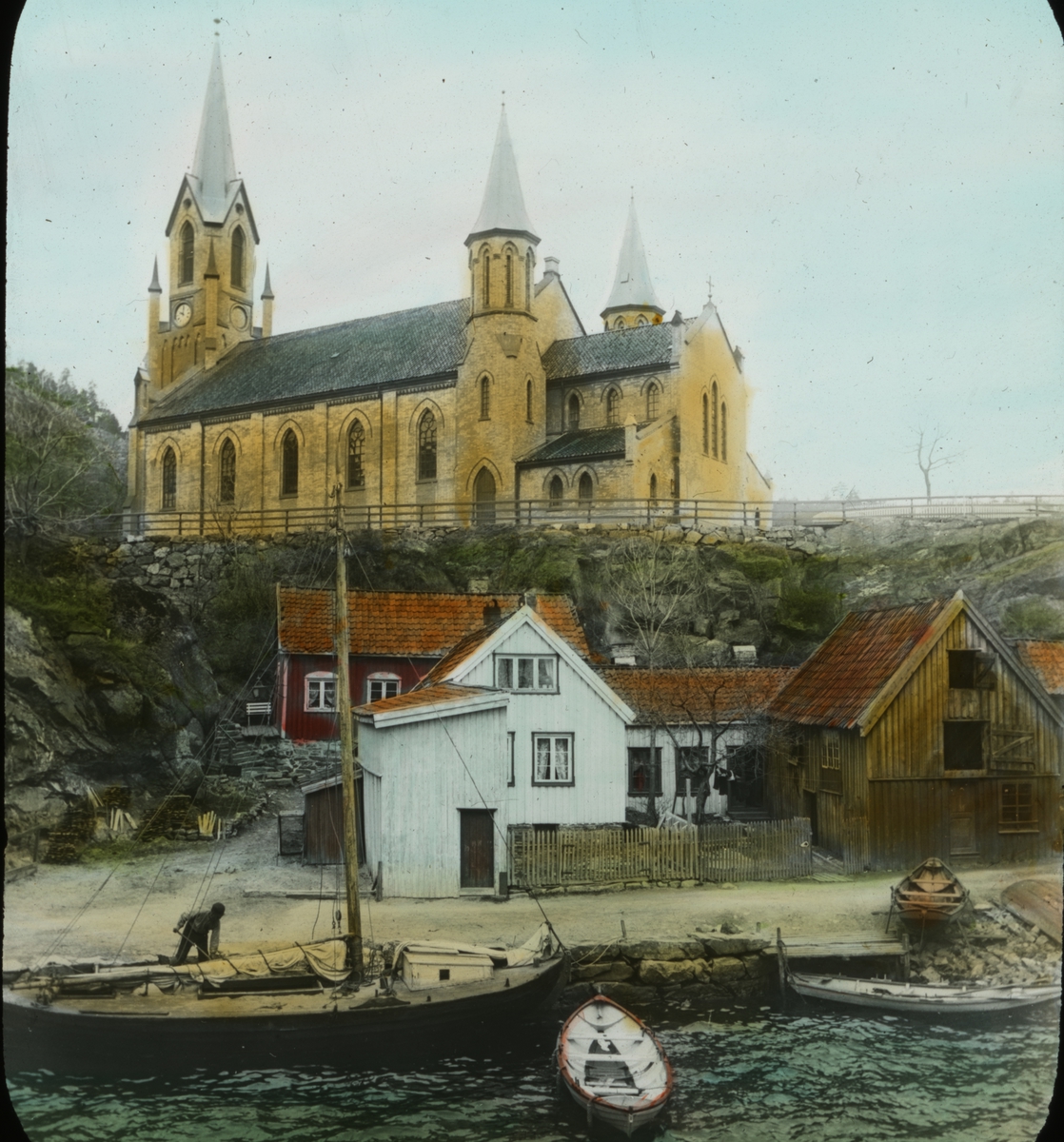 Kragerø kirke sett fra Kirkebukta.Hus, prammer og en seilbåt i forgrunn