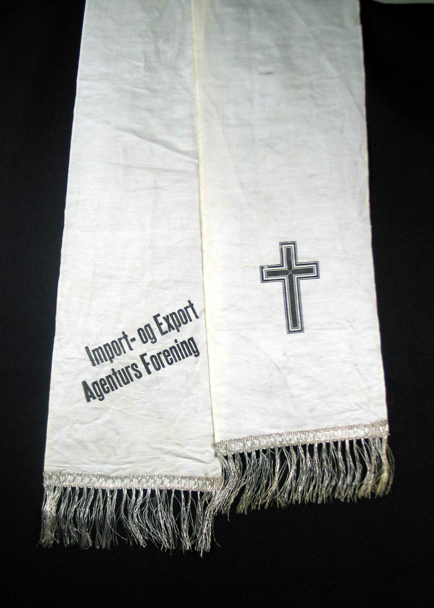 Begravelsessløyfe i hvit silke med svart tekst og sølvfrynser.