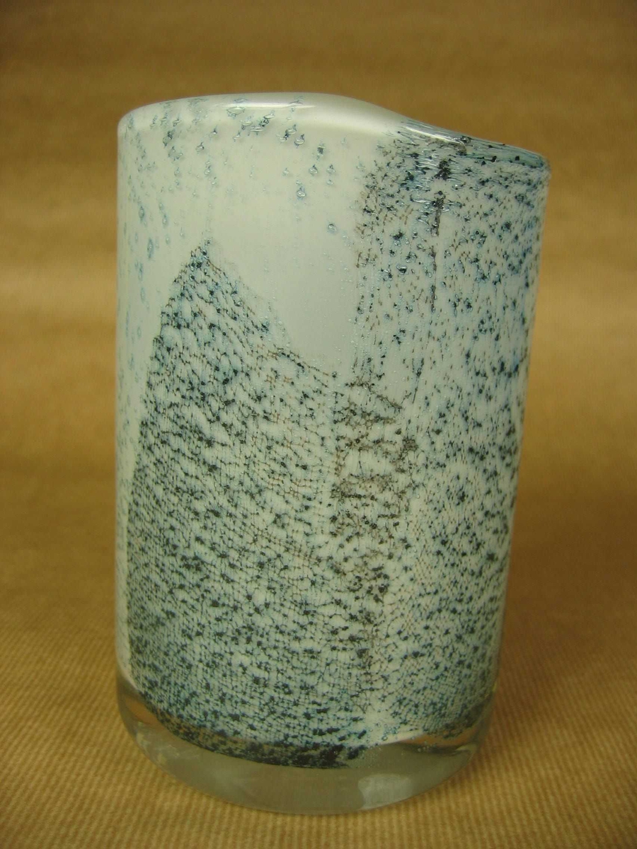 Sylindrisk glassvase av hvitt glass med klart overtrekk. Dekor av blå fiberduk.