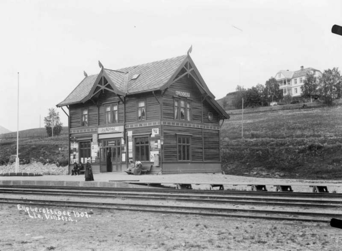 Kort: Sør- Fron, Hundorp jernbanestasjon.16.06.1907. Bygning, jernbaneskinner, reisende, villa i bakgrunnen.