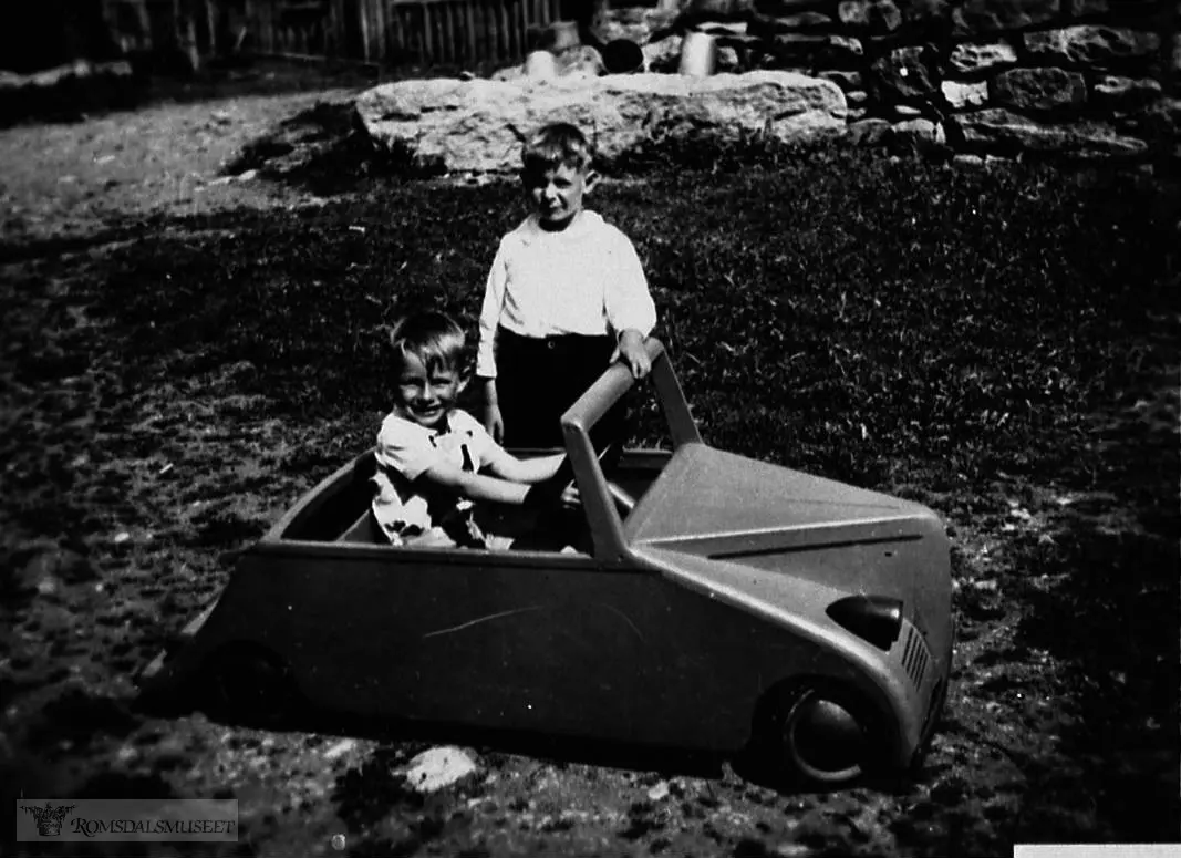 Bjørn Oppigard som sjafør og Tora Oppigard som passasjer i leikebilen. Bilen var laga av Tore Vassli til Bjørn sin 5 års-dag 28.05.1944...