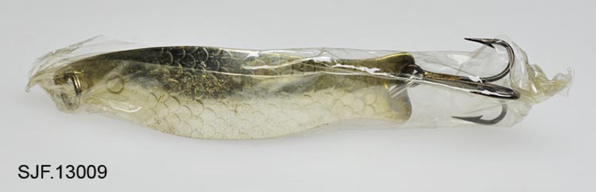 Sluken er en dorgeskje av typen Brisling, produsert av den norske slukfabrikanten Delfin. Den er pakket i cellofan, trolig produsentens forpakning, og derfor sannsynligvis ubrukt.  Dorgeskjeen er laget av et flatt metallstykke som er formet i en bue. Den har et fiskeskjellmønster og et øye på utsiden, på innsiden har den en blank messingfarge og innskrifter (avskrevet i eget felt). Dorgeskjeen er utstyrt med to splittringer, en i hver ende. I den ene er det festet en treblekrok, i den andre festes senen. Noe rust på splittringer og krok. Sluken er for lett til å kaste, den brukes til dorgefiske, det vil si at den trekkes etter båt. 