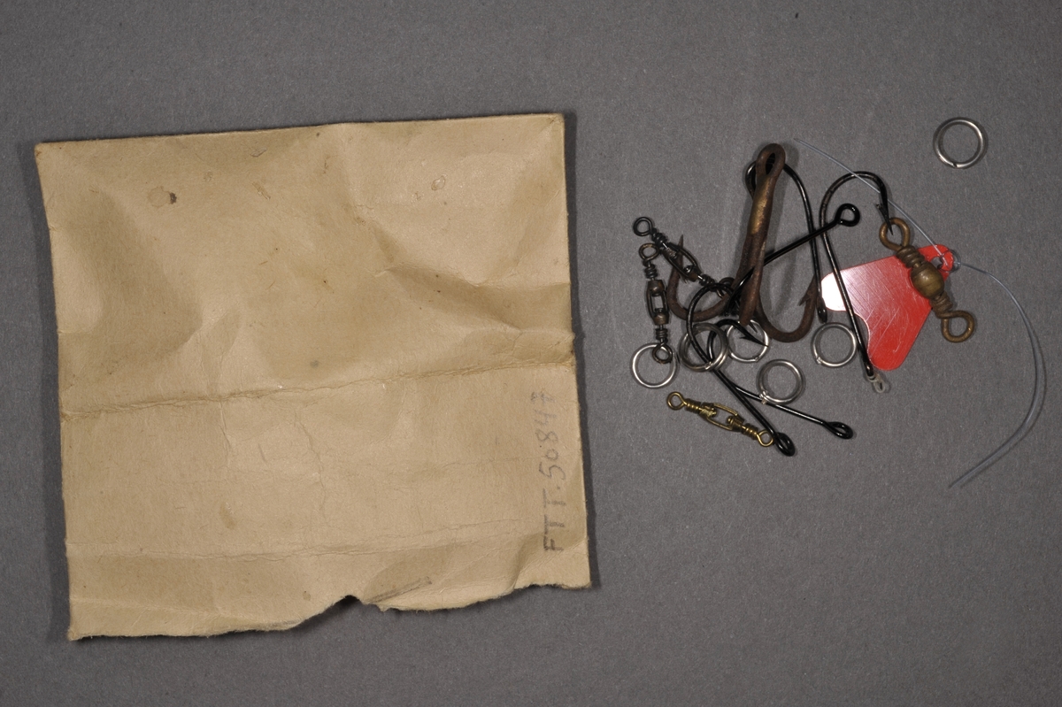 Liten papirpose med småutstyr til fiske. Fem enkle kroker, fem spinnere, seks splittringer, en rød plastspinner, og en treleddet krok.