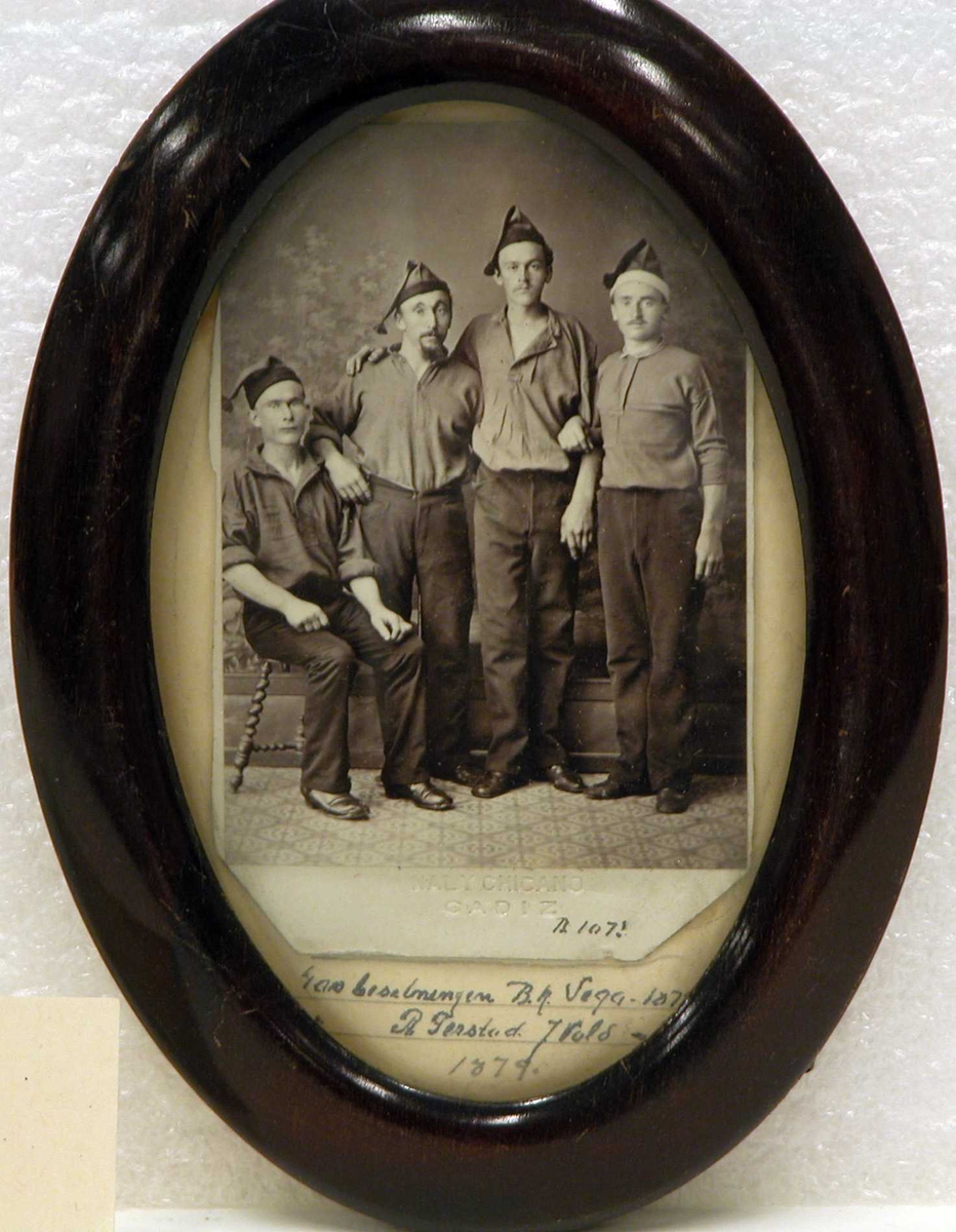 4 menn står oppstilt for fotografering i like bukser, skjorter og toppluer.(en sitter på stol). De er fire av besetningen på barken "Vega". Bildet tatt i 1879.