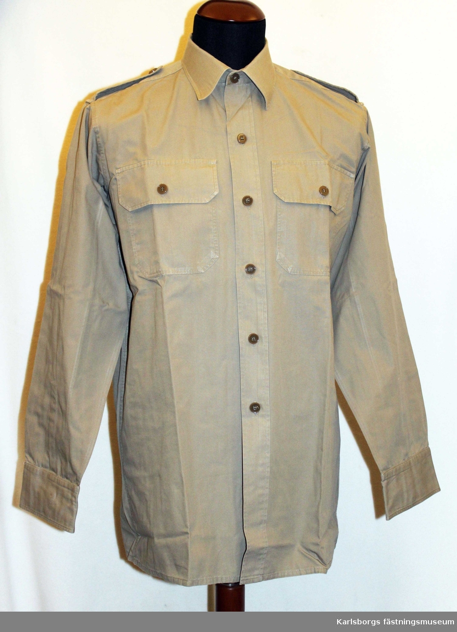 Skjorta m/1952 avsedd för tropikdräkt. Långärmad, med nedvikt krage, påstickade bröstfickor med knäppara ficklock. Har använts vid FN tjänstgöring. Storlek 39.