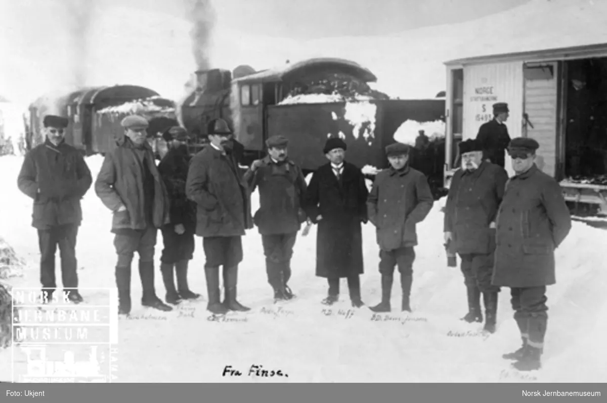 NSBs ledelse på plattformen på Finse stasjon med et snøryddingstog i bakgrunnen under blokaden av Bergensbanen i påsken 1913