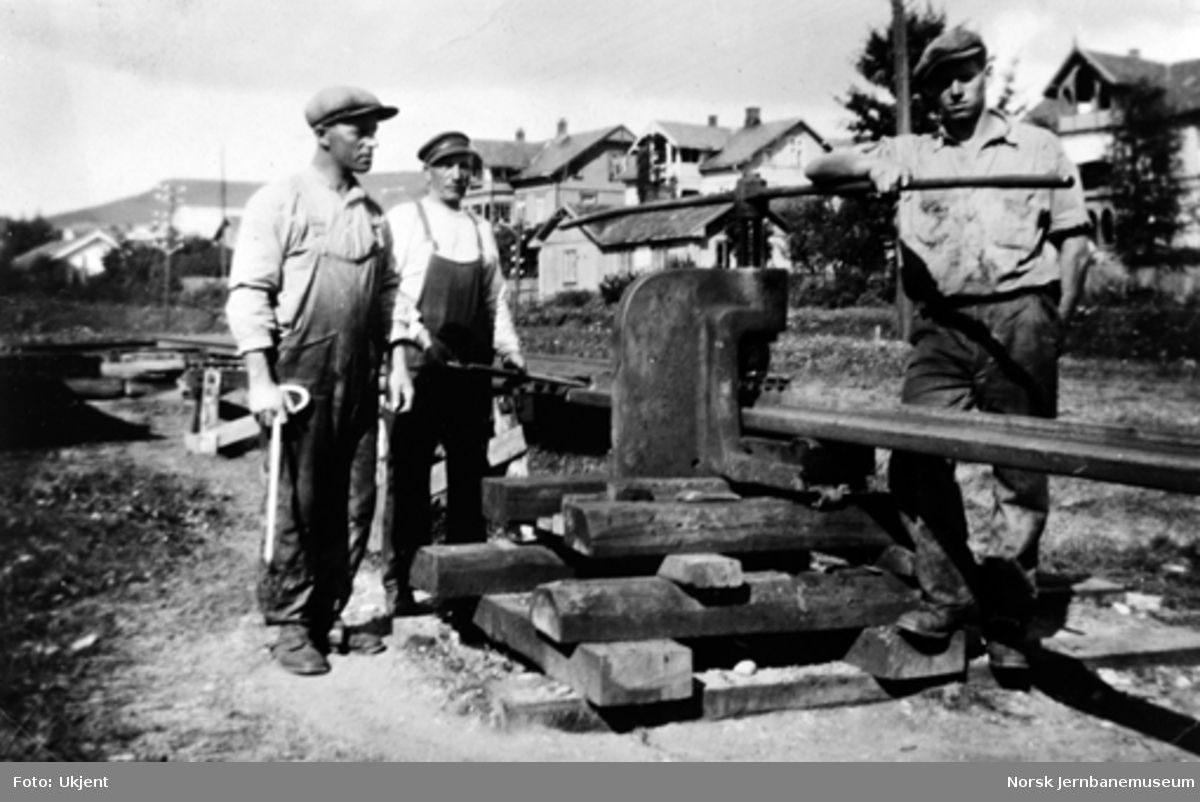 Tre banearbeidere ved en skinnepresse