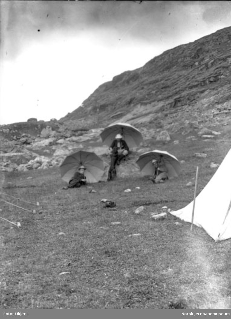 Tre menn ved en teltleir for stikningspersonalet