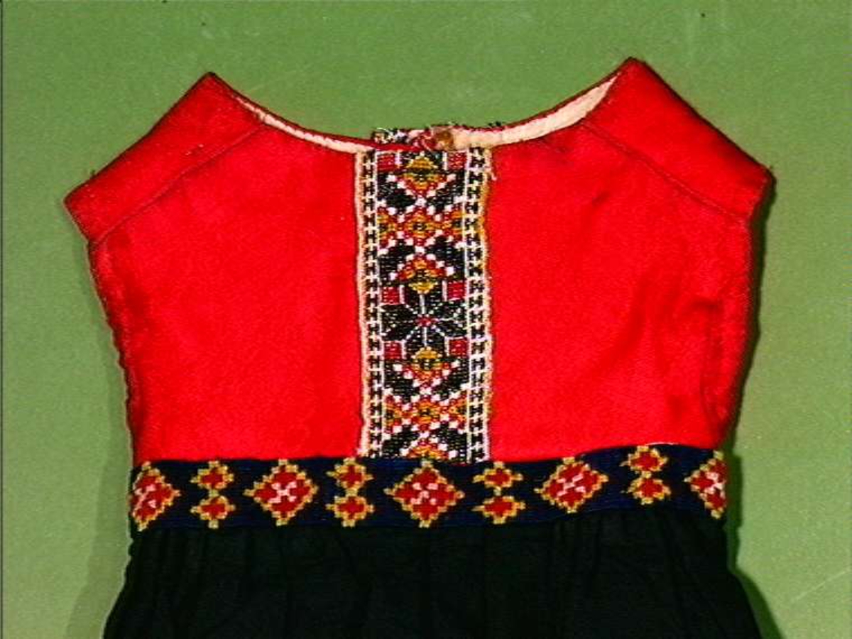 Lue til jente i rød ulldamask med dekor av kniplad metallblonde, silkebånd, broderi og applikasjoner.