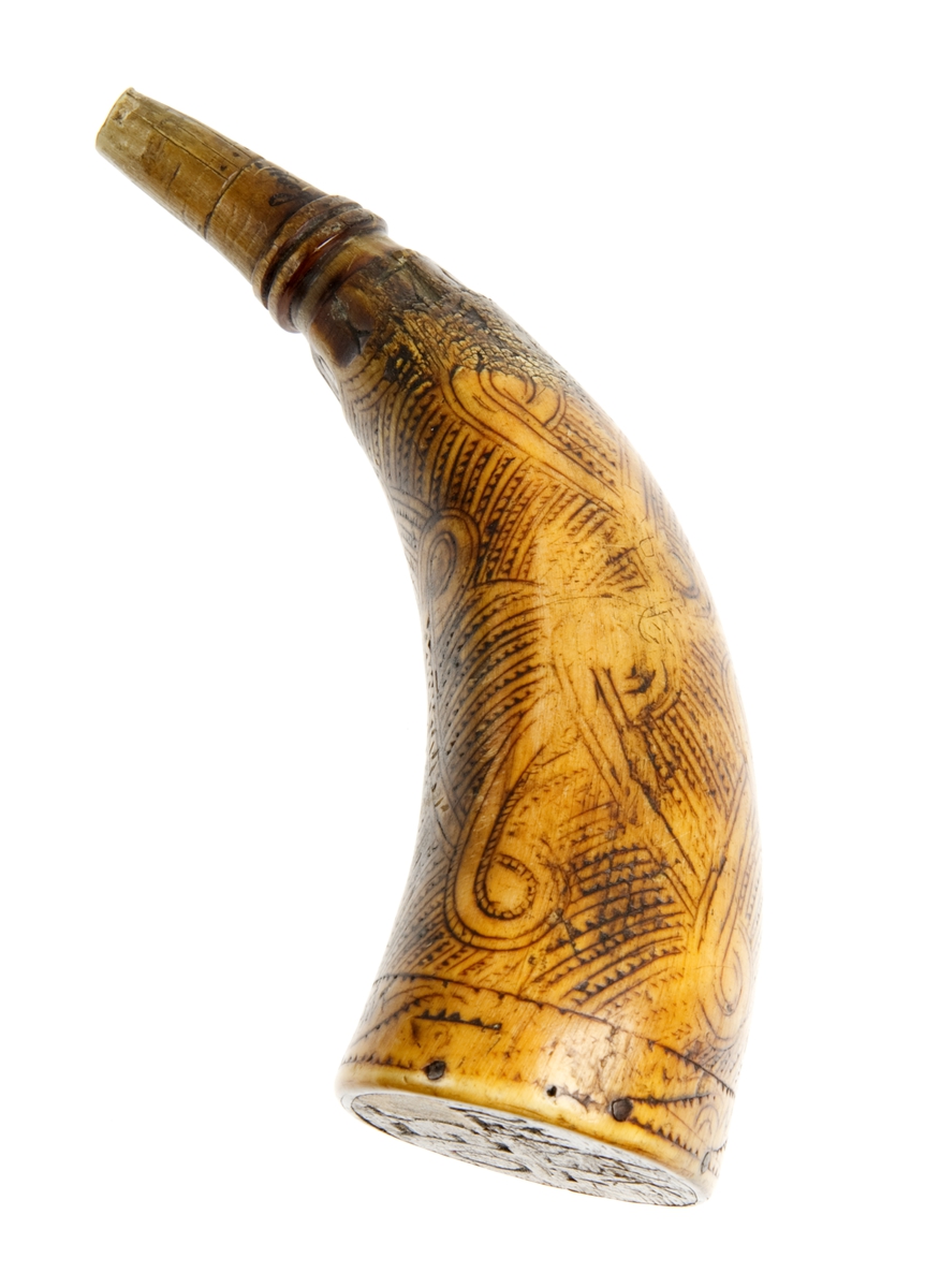 Krutthorn med flat bunnplate i tre med innskrift. Ornamentikk på horn i form av et bånd som går i løkker over hornet mot en bakgrunn av streker med hakk.