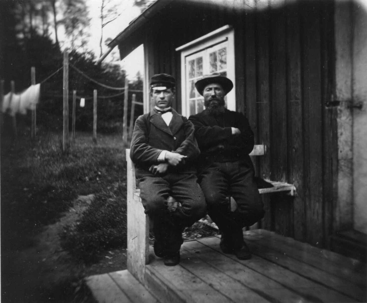 Husmannsfolk, to menn på benk foran  hus.
Fra portrettserie av personer som bodde på eller besøkte Dal gård, Ullensaker, fotografert av gårdens eier, kammerherre Fredrik Emil Faye (1844-1903) i årene 1875-1900.