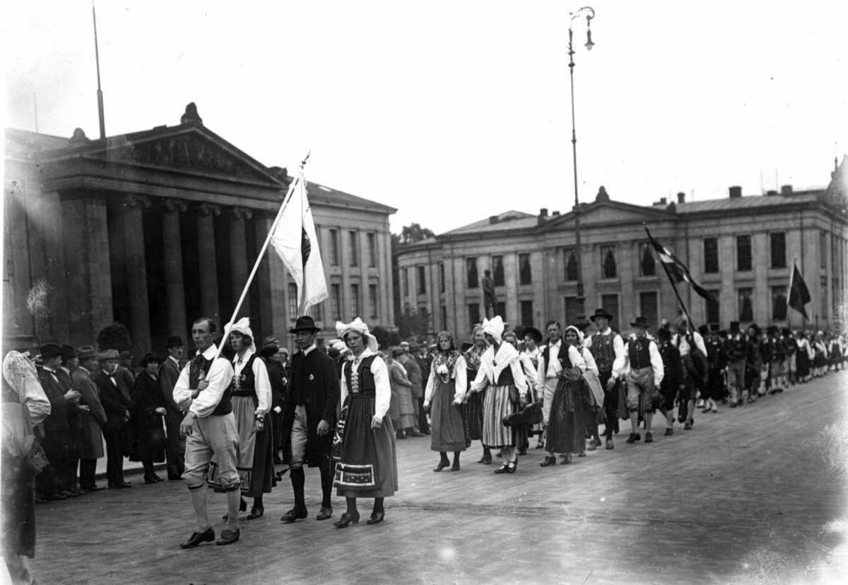Nordisk Folkedansstevne. Karl Johans gate ved Universitetet - Oslo. 1925. Opptog av norske og svenske folkedansere. Flagg. Publikum.