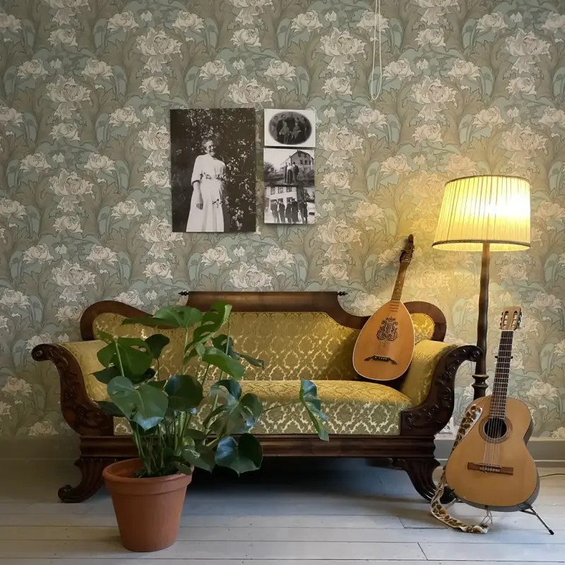 En biedermeier-sofa med gult trekk i et rom med blomstrete tapet og gråmalt tregulv. I sofaen står en lutt, på gulvet står en gitar, en stålampe og en monstera i potte.